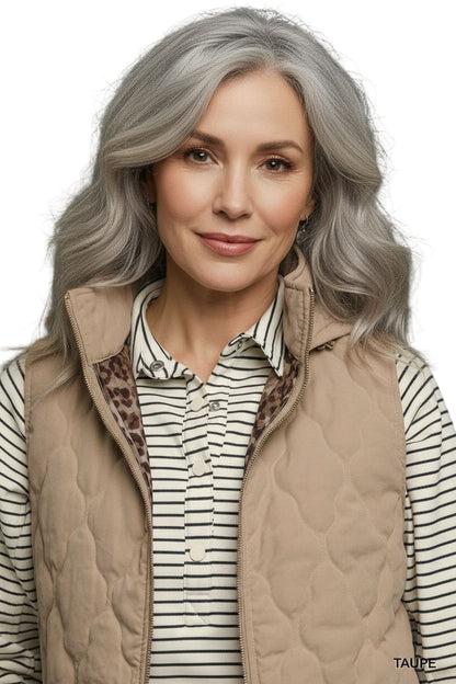 Woman wearing a beige quilted vest over a striped shirt with a gray background